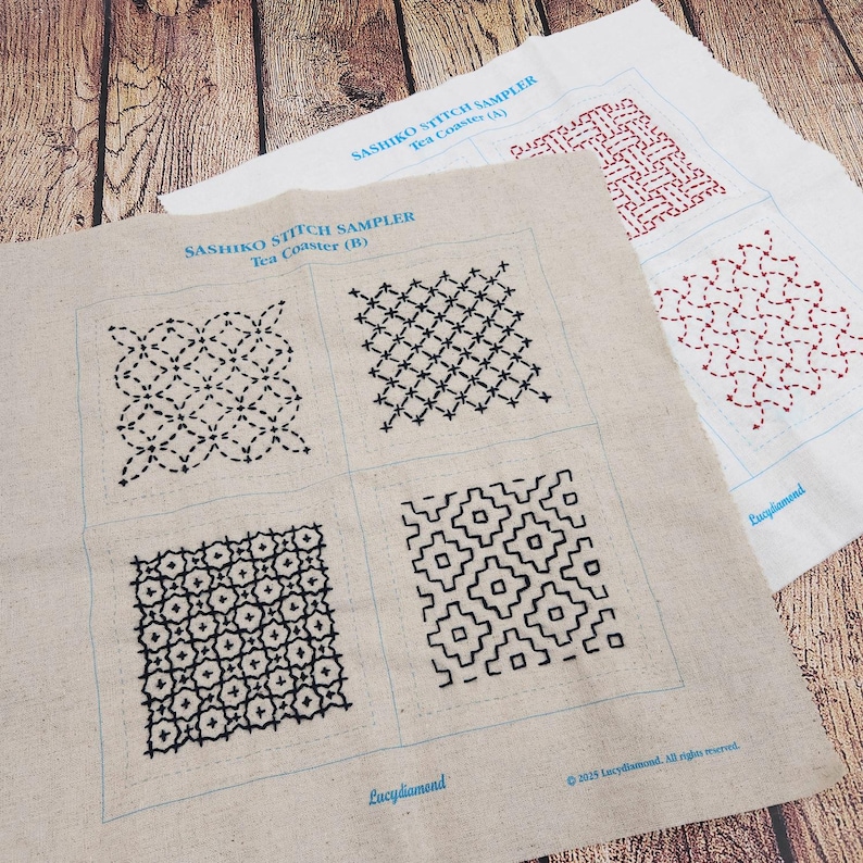 May include: Two rectangular fabric panels featuring Sashiko stitch sampler patterns. The top panel is white with red stitching, while the bottom panel is beige with black stitching. Both include blue printed text labels and grid outlines.