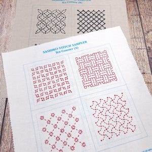 May include: Two off-white fabric squares featuring Sashiko stitch sampler patterns. The top piece is labeled Tea Coaster (B) with black geometric designs. The bottom piece is labeled Tea Coaster (A) with red geometric designs and the text Lucydiamond.