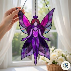 May include: A stained glass fairy with purple and pink wings, a crown, and a glittery bodice. The fairy is hanging from a black chain. The background includes a window with white curtains and a basket of white flowers.