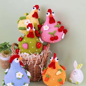 以下が含まれることがあります： バスケットに入った、カラフルなかぎ針編みのニワトリの置物と、陶器のウサギ。ニワトリは黄色、ピンク、緑、青、オレンジなど様々な色で、花、イチゴ、サクランボで飾られています。