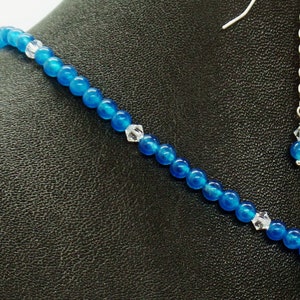 May include: A close-up of a blue beaded necklace and earring set. The necklace features small, round, bright blue beads interspersed with clear crystal accents. The earrings have a matching blue bead and crystal.