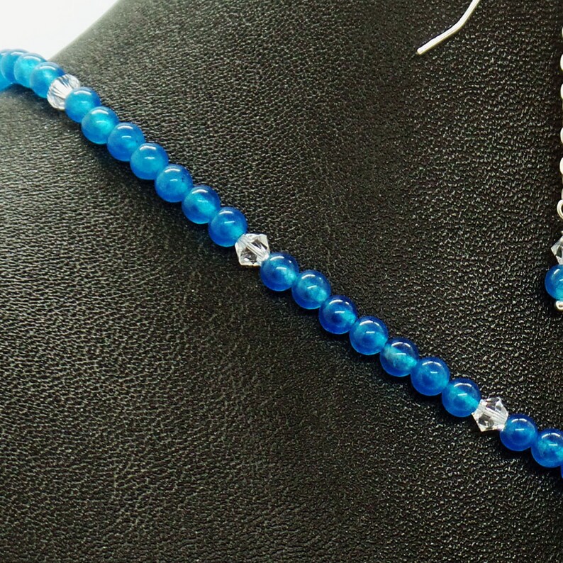 May include: A close-up of a blue beaded necklace and earring set. The necklace features small, round, bright blue beads interspersed with clear crystal accents. The earrings have a matching blue bead and crystal.