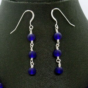 May include: A pair of silver dangle earrings with four dark blue glass beads on each earring.