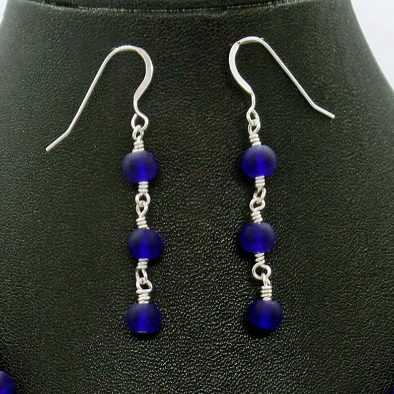 May include: A pair of silver dangle earrings with four dark blue glass beads on each earring.