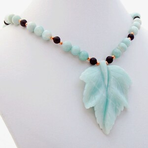 May include: A light blue and black necklace with a carved leaf pendant. The necklace is made of round beads and features a carved leaf pendant made of the same light blue stone.