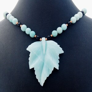 May include: A light blue carved leaf pendant necklace with black and copper beads.