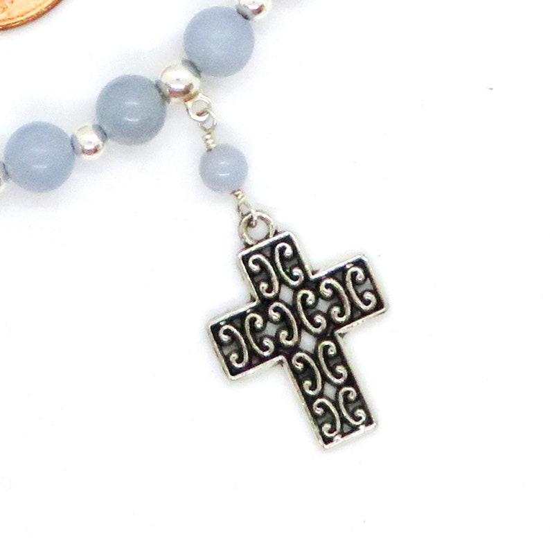 May include: A close-up of a rosary with light blue beads and a decorative silver cross pendant. The cross features an openwork design. The rosary is on a white background.
