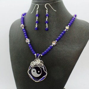 May include: A silver necklace with a blue glass yin yang pendant and matching earrings. The necklace is made with blue glass beads and silver wire.