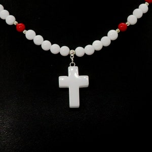May include: White cross pendant necklace with a beaded design. The necklace features a white cross pendant suspended from a strand of white and red beads. The beads are round and evenly spaced, creating a simple yet elegant design.
