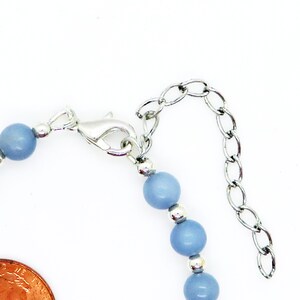 May include: A close-up of a bracelet with light blue beads and silver-colored metal accents. The bracelet has a lobster clasp and an adjustable chain. The beads are round and evenly spaced.