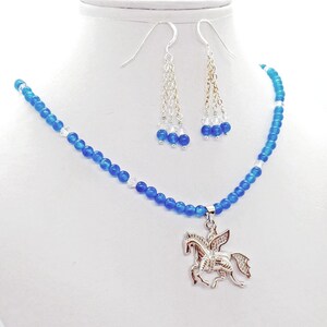 May include: A blue beaded necklace with a silver Pegasus pendant and matching earrings. The earrings have dangling chains with blue and clear beads. The necklace and earrings are displayed on a white mannequin.