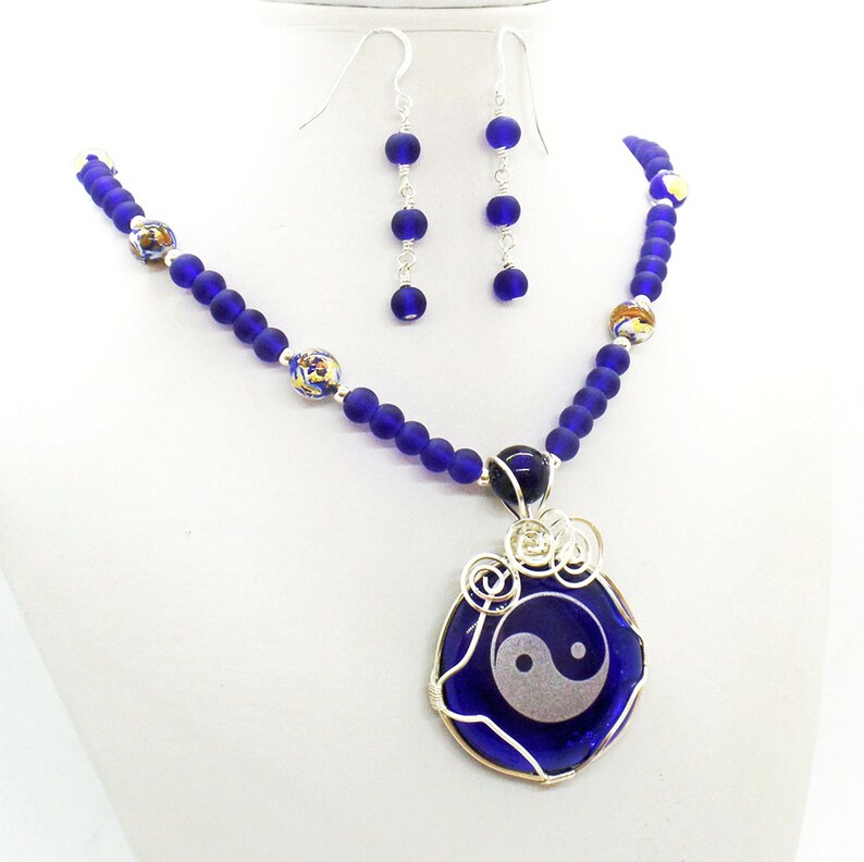 May include: A blue glass necklace with a yin yang pendant and matching earrings. The necklace features blue and gold glass beads.