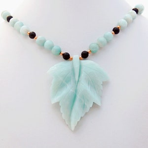 May include: A light blue carved leaf pendant necklace with black and gold beads.