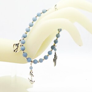 May include: A light blue beaded bracelet with silver-colored charms, including a heart, cross, and anchor. The bracelet features round, light blue beads and small silver beads. The charms are detailed and dangle from the bracelet.