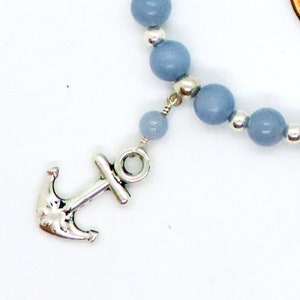 May include: A nautical-themed bracelet featuring light blue beads and a silver-colored anchor charm. The beads are strung together with silver accents, creating a simple yet elegant design. The anchor charm adds a maritime touch to the jewelry.