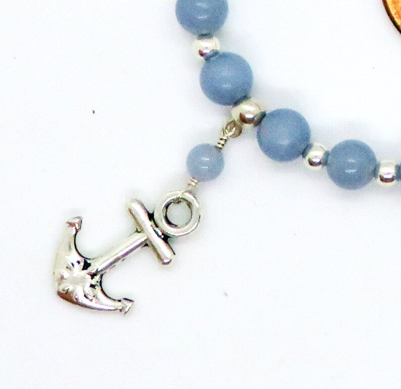 May include: A nautical-themed bracelet featuring light blue beads and a silver-colored anchor charm. The beads are strung together with silver accents, creating a simple yet elegant design. The anchor charm adds a maritime touch to the jewelry.
