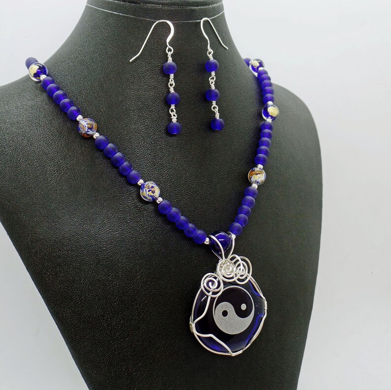 May include: A necklace with a yin yang pendant and blue glass beads. The necklace is paired with matching earrings.