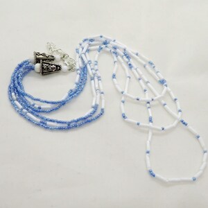 May include: A collection of beaded necklaces in shades of white and blue. One necklace is a multi-strand design with silver-toned clasps. The other necklace is a long, single-strand design. The beads are small and evenly spaced.