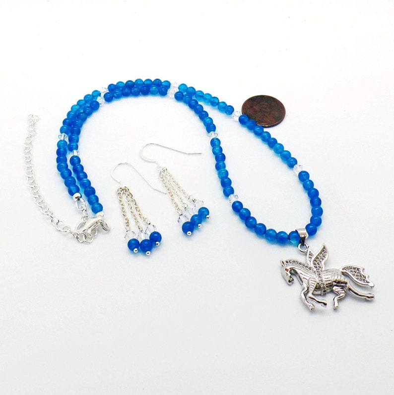 May include: A blue beaded necklace and matching earrings set. The necklace features a silver Pegasus pendant. The earrings have dangling chains with clear and blue beads. The jewelry set is on a white background.