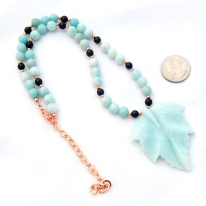 May include: A turquoise and black beaded necklace with a carved turquoise leaf pendant. The necklace is made with round beads and has a lobster clasp closure.