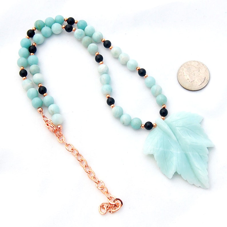 May include: A turquoise and black beaded necklace with a carved turquoise leaf pendant. The necklace is made with round beads and has a lobster clasp closure.