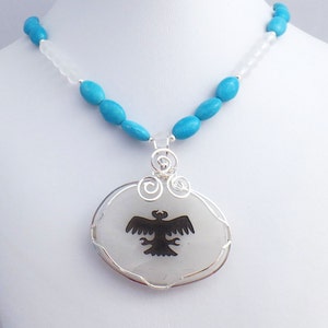 May include: A turquoise and white beaded necklace with a silver pendant featuring a black silhouette of an eagle on a white stone.