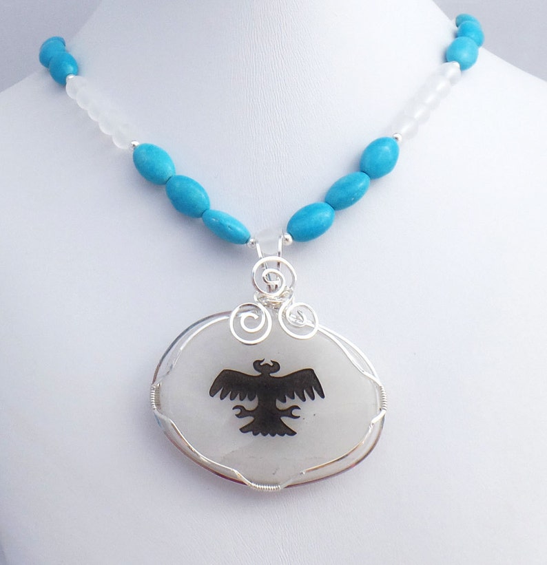May include: A turquoise and white beaded necklace with a silver pendant featuring a black silhouette of an eagle on a white stone.