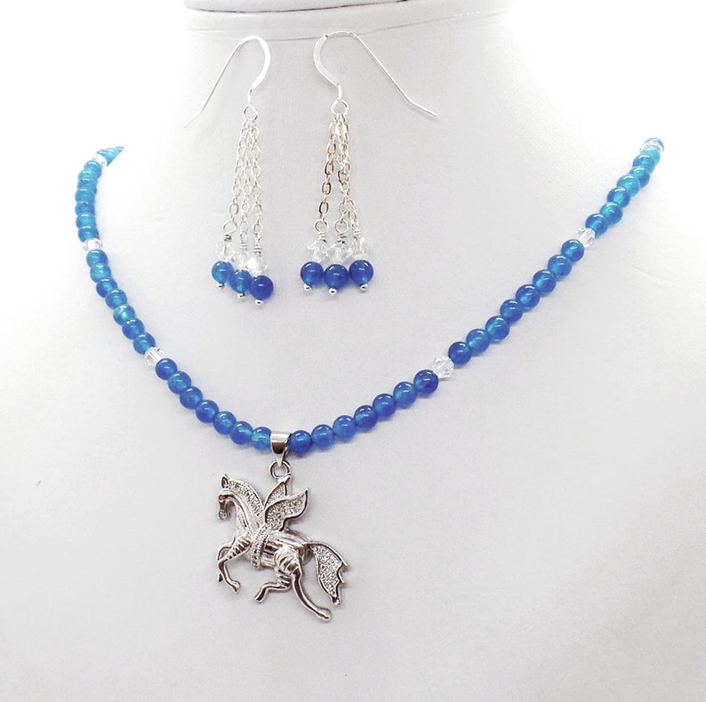 May include: A jewelry set featuring a blue beaded necklace with a silver Pegasus pendant, and matching dangle earrings. The earrings and necklace have clear and blue beads. The Pegasus pendant is detailed with clear stones.