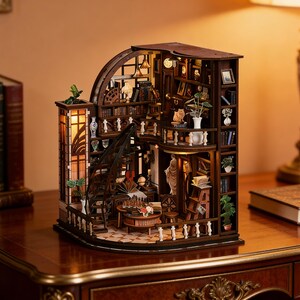 May include: A multi-level wooden miniature library book nook kit featuring a spiral staircase, bookshelves filled with tiny books, a desk with a chess set, a balcony with a statue, and integrated warm lighting throughout the structure.