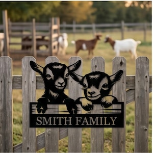 May include: A black metal sign featuring two goat kids peering over a horizontal bar, with the text SMITH FAMILY printed in capital letters below. The design is mounted on a wooden fence, showcasing a detailed silhouette of the young goats.