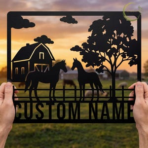 Puede incluir: Arte de pared de metal negro con un granero, dos caballos, un árbol y nubes contra un fondo de puesta de sol. Las palabras "CUSTOM NAME" están recortadas en la parte inferior. Una pieza decorativa para un hogar o granja.