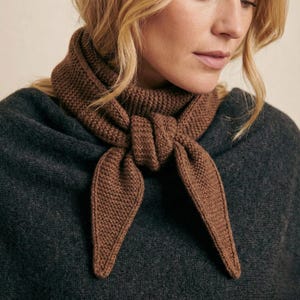 以下が含まれることがあります： 茶色のニットスカーフは結び目になっており、長く尖った端があります。 スカーフは太く、質感のある糸でできており、濃い灰色のセーターの上に着用されています。 スカーフは暖かく居心地の良いアクセサリーです。
