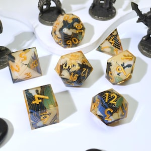 May include: A selection of multi-sided dice with a distinctive design. The dice are made of clear resin with a blue, green, and gold pattern. The numbers are gold. Metal figurines are in the background.
