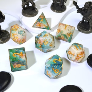 May include: A collection of colorful, floral-themed polyhedral dice. The dice are transparent with gold numbering and feature pink and blue floral designs. Miniature figurines are in the background.