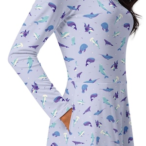 May include: A light purple dress with long sleeves and pockets, patterned with various sea creatures in shades of blue and purple. The dress features a fitted bodice and a flared skirt, suitable for casual wear.