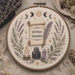 May include: An embroidery hoop featuring a cream fabric background with a central scroll displaying the text Written Intention. A purple quill, a lit candle, an ink bottle, and a crystal are surrounded by lavender sprigs and moon phases.