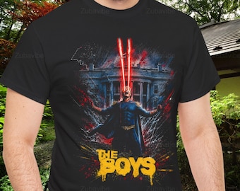 May include: A black short-sleeved t-shirt featuring a graphic print of a character in a blue suit with a cape, emitting red laser beams from their eyes in front of a white building. The text THE BOYS is printed in yellow at the bottom of the graphic.