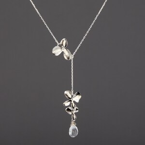 May include: A silver necklace with a delicate chain and two silver flower charms. The necklace has a single clear crystal pendant hanging from the bottom.