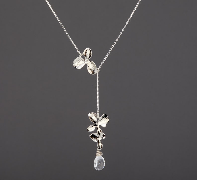 May include: A silver necklace with a delicate chain and two silver flower charms. The necklace has a single clear crystal pendant hanging from the bottom.