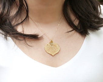 Puede incluir: Un collar de oro con una cadena delicada y un colgante en forma de hoja. El colgante está hecho de oro texturizado y tiene un diseño detallado.