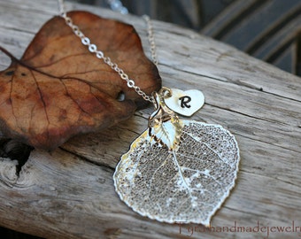 Puede incluir: Un collar de plata con una cadena delicada y un colgante con una hoja de álamo real, preservada, con un dije de corazón de plata con la letra "R" grabada.
