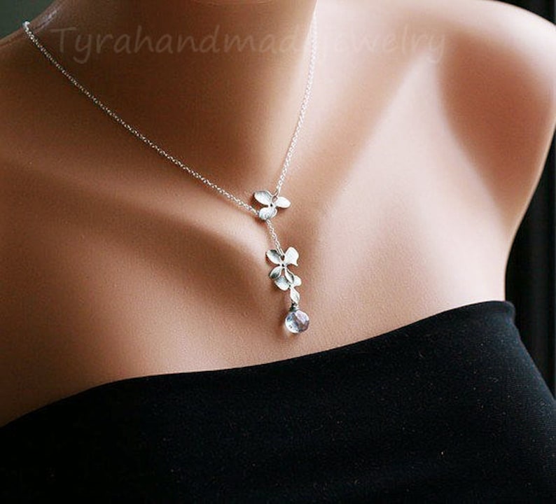 May include: A silver necklace with a delicate flower design and a clear gemstone pendant. The necklace is on a model's neck.