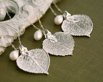Puede incluir: Cuatro collares de plata con delicados colgantes de hojas y detalles de perlas blancas. Los collares se muestran sobre un fondo blanco.