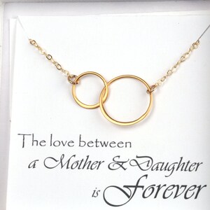 May include: Gold necklace with two interlocking circles, presented in a white box with the inscription "The love between a Mother & Daughter is forever".