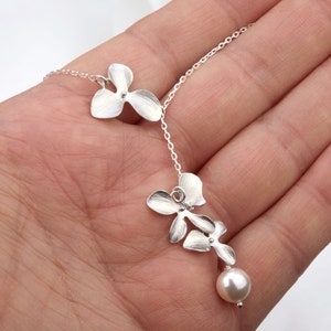 May include: A silver necklace with a delicate chain and three flower-shaped pendants. The pendant at the bottom is a pearl.