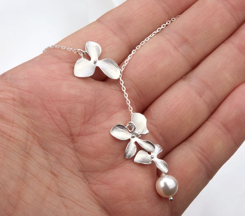 May include: A silver necklace with a delicate chain and three flower-shaped pendants. The pendant at the bottom is a pearl.
