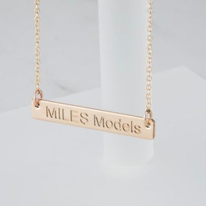 May include: Gold necklace with a bar pendant that says "MILES Models".