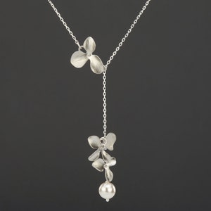 May include: A silver necklace with a delicate chain and two flower-shaped pendants. The bottom pendant has a pearl attached.