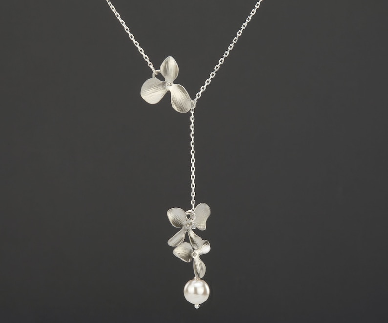 May include: A silver necklace with a delicate chain and two flower-shaped pendants. The bottom pendant has a pearl attached.