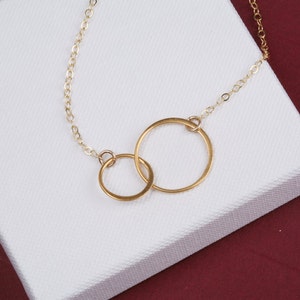 May include: A gold chain necklace with two interlocking circles as a pendant.